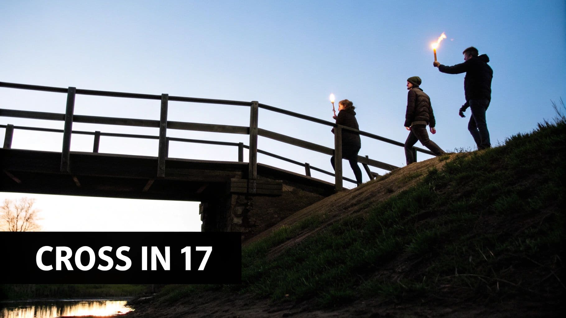 Three people with lit torches walk uphill towards a bridge at dusk, reflected in water below.