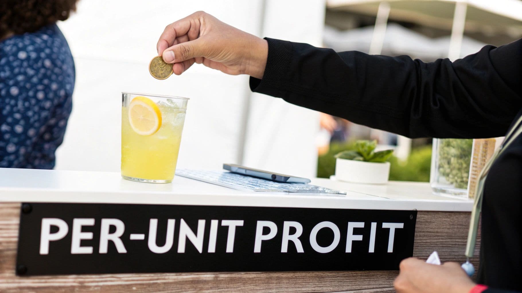A hand drops a coin into a glass of lemonade on a counter, with a 'PER-UNIT PROFIT' sign below.